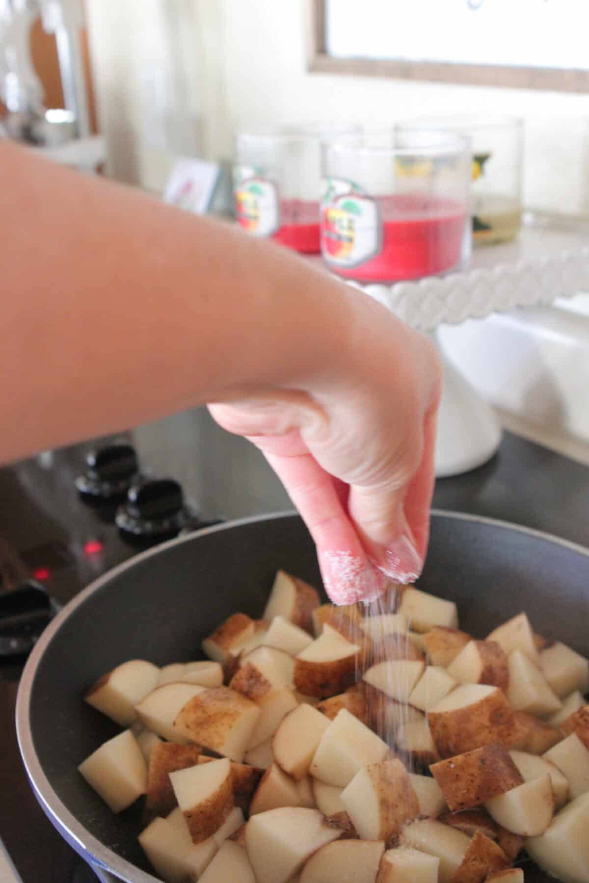 seasoning cubed potatoes with salt in skillet