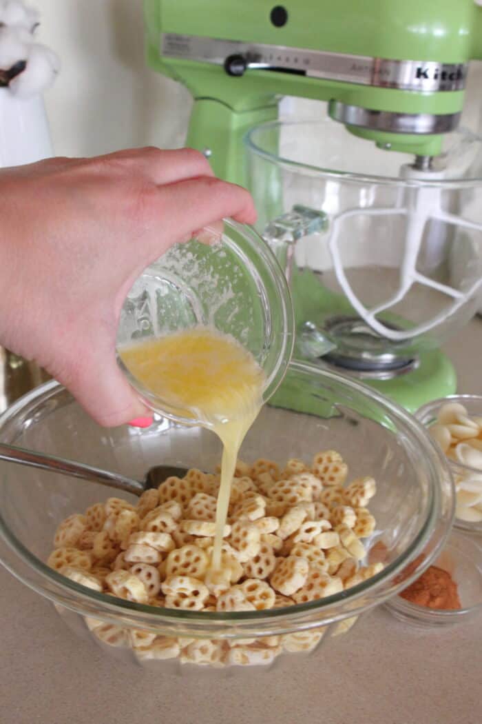 pouring melted butter into honey comb cereal in mixing bowl