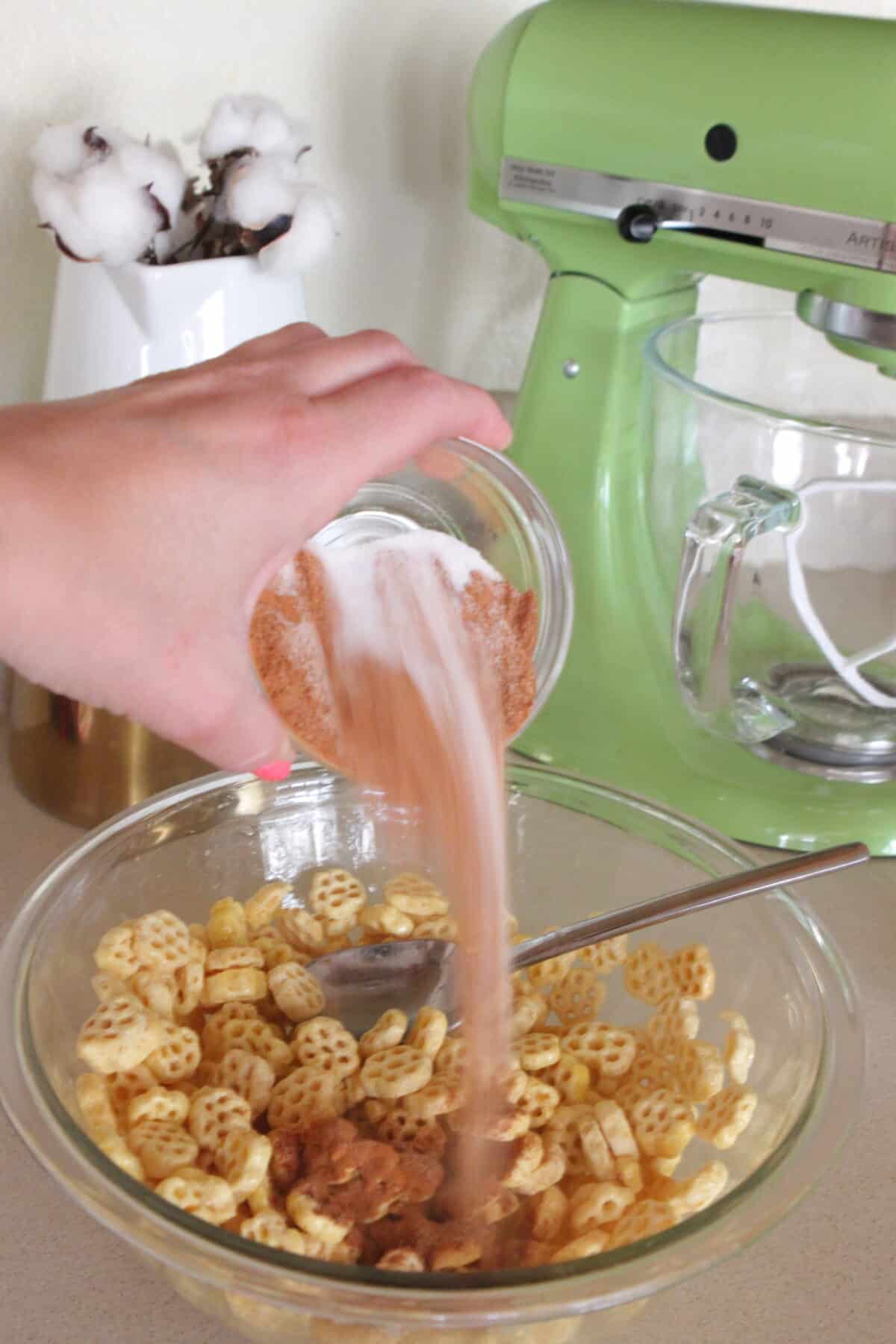 adding cinnamon sugar over cereal mixture in mixing bowl