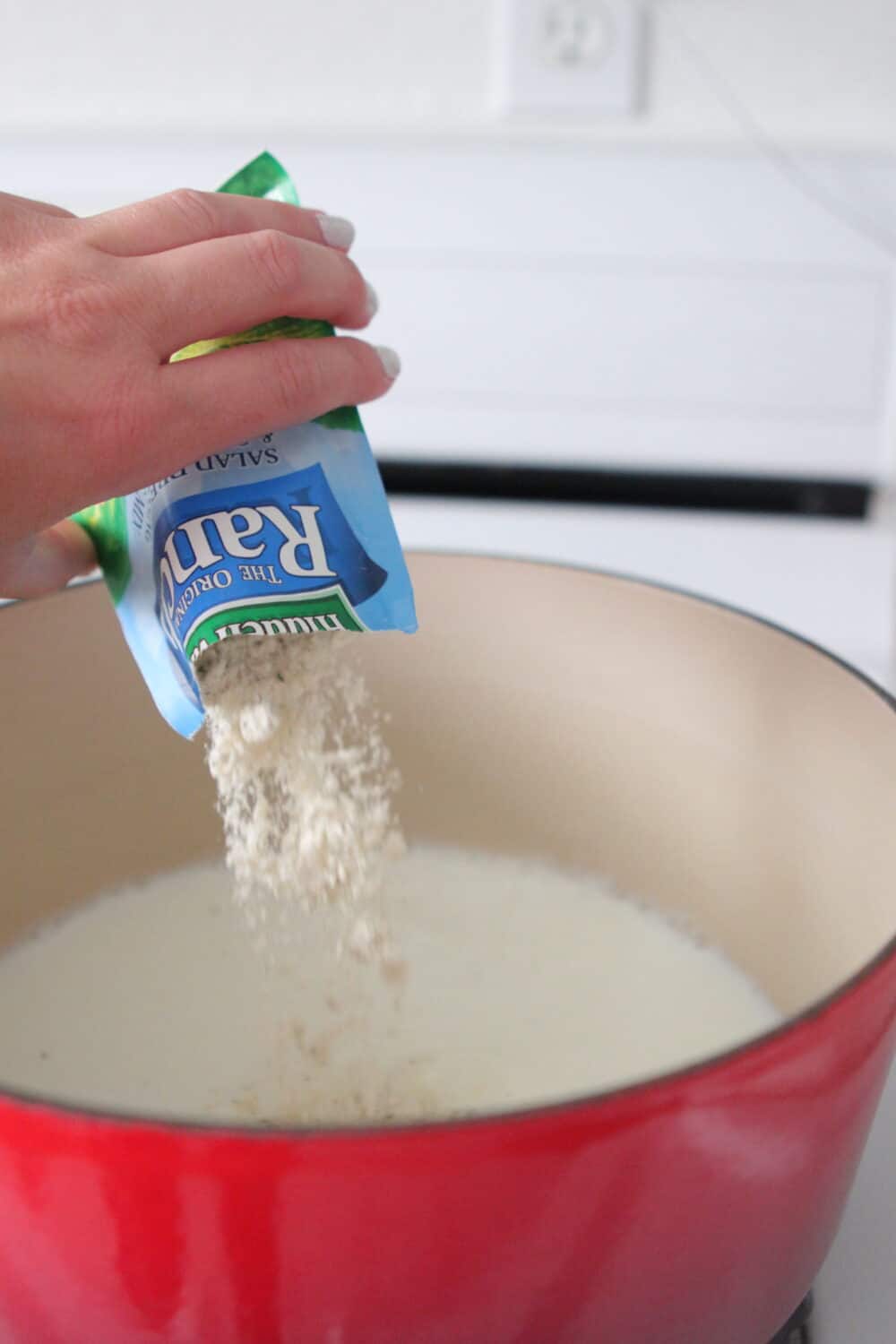 pouring ranch dressing seasoning into pot for sauce