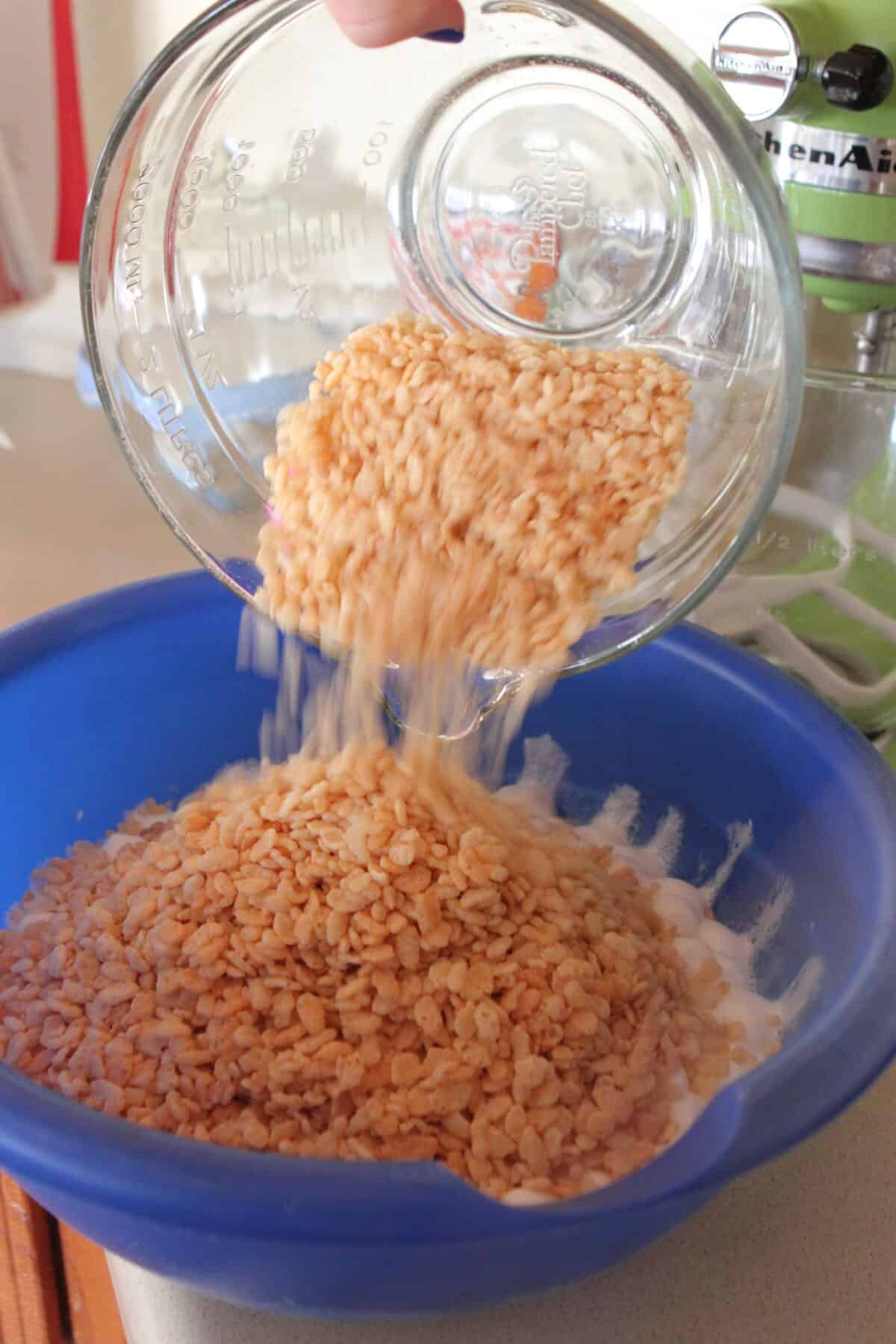 pouring rice krispie cereal into melted marshmallows in mixing bowl