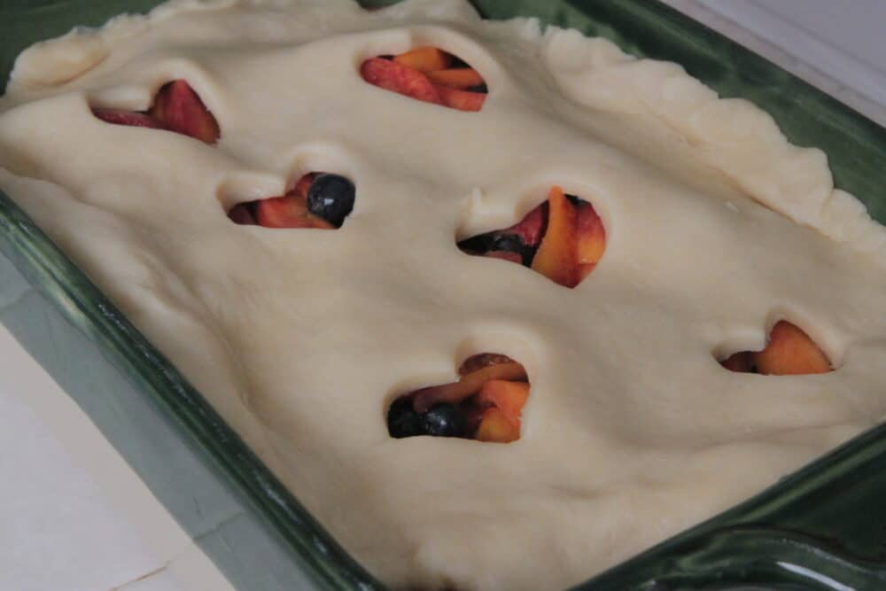 pouring fruit filling into homemade cobbler pie dough