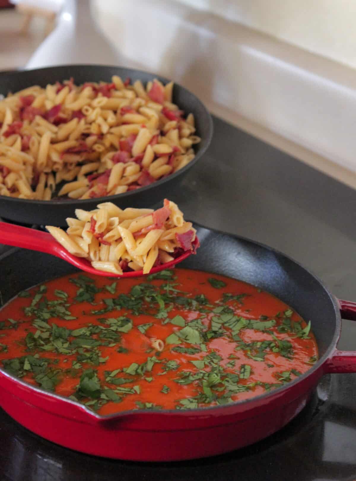 adding pasta to tomato sauce in large skillet