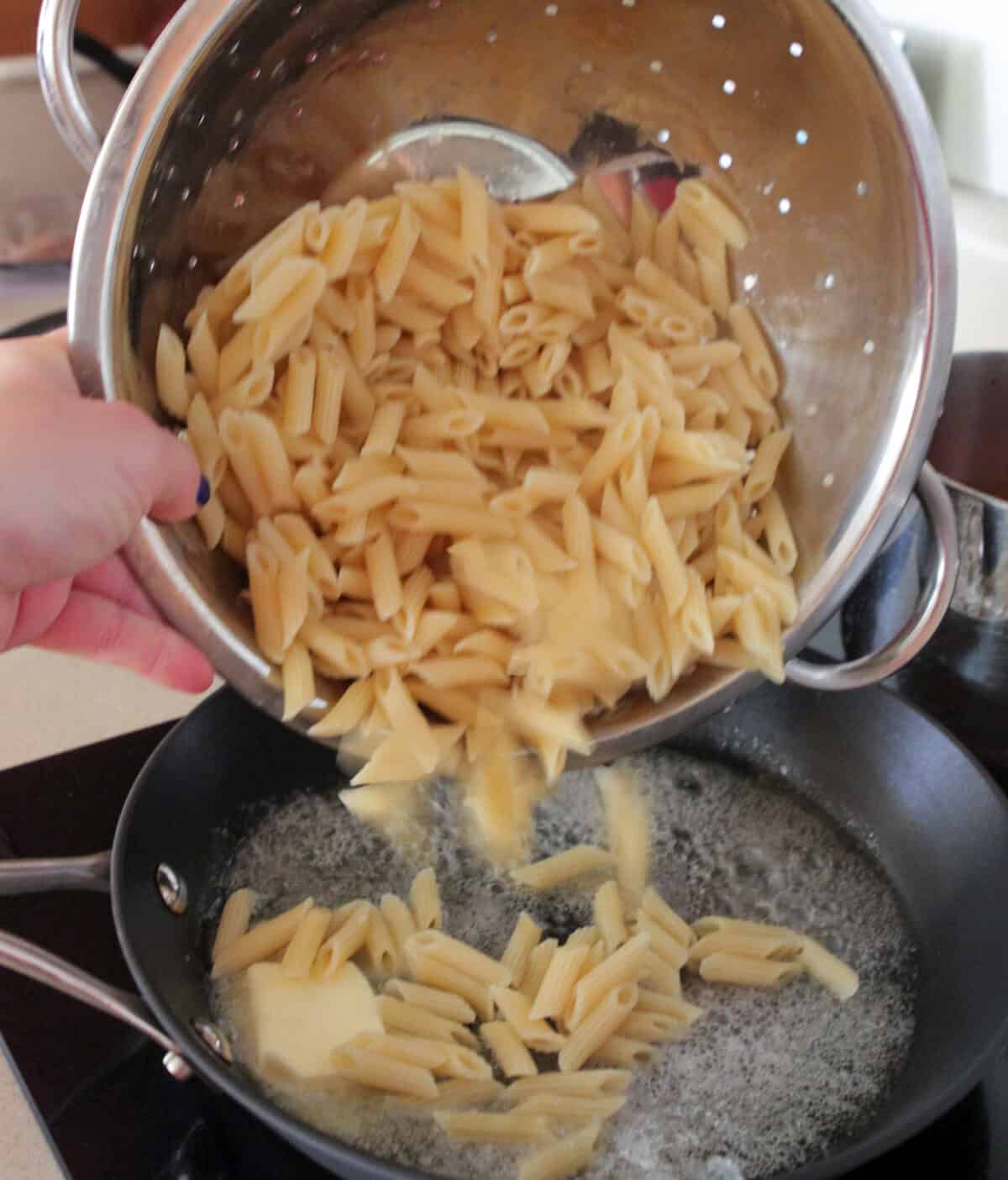 pouring cooked penne pasta in skillet on stovetop