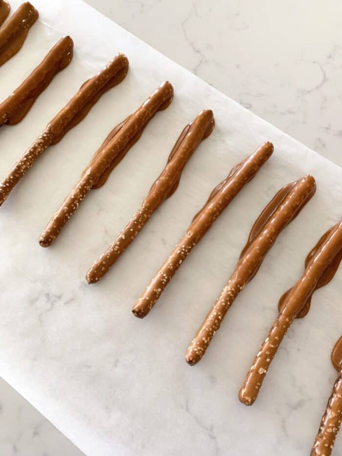 caramel dipped pretzel rods on parchment paper