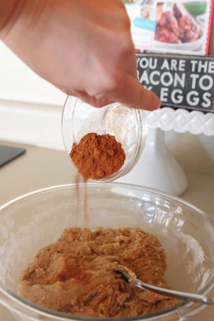 pouring cinnamon into mixing bowl for cinnamon cookies