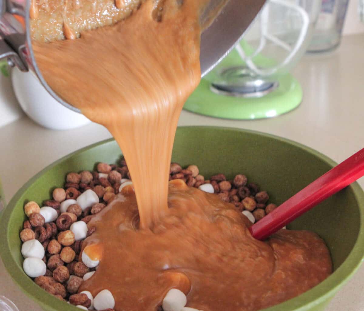 pouring peanut butter sauce over cereal mixture in mixing bowl