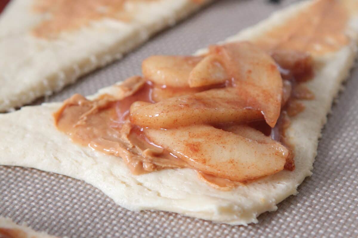 apples and peanut butter spread over crescent roll on baking sheet