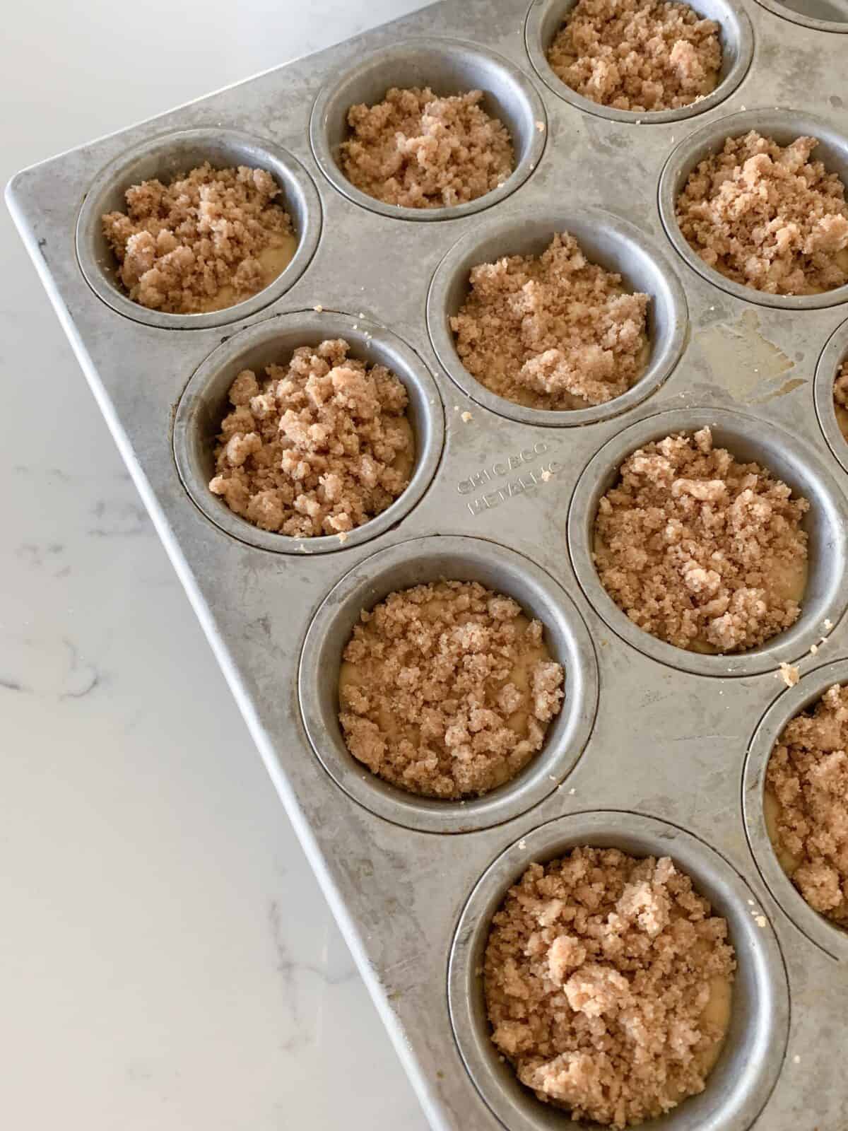 streusel topping on pumpkin muffin batter in muffin tin