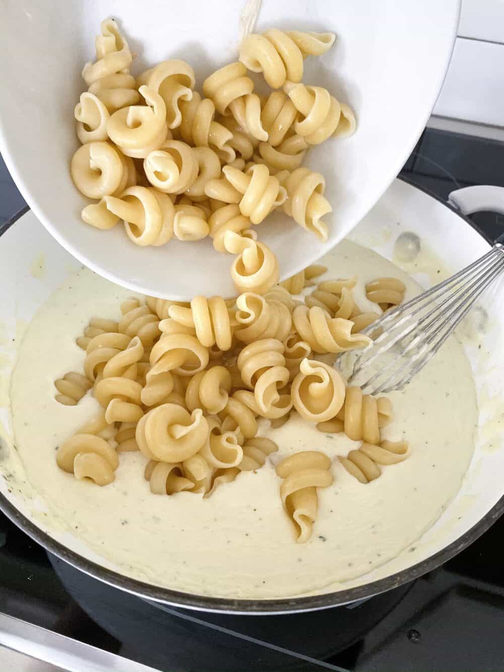 adding cooked pasta to alfredo sauce