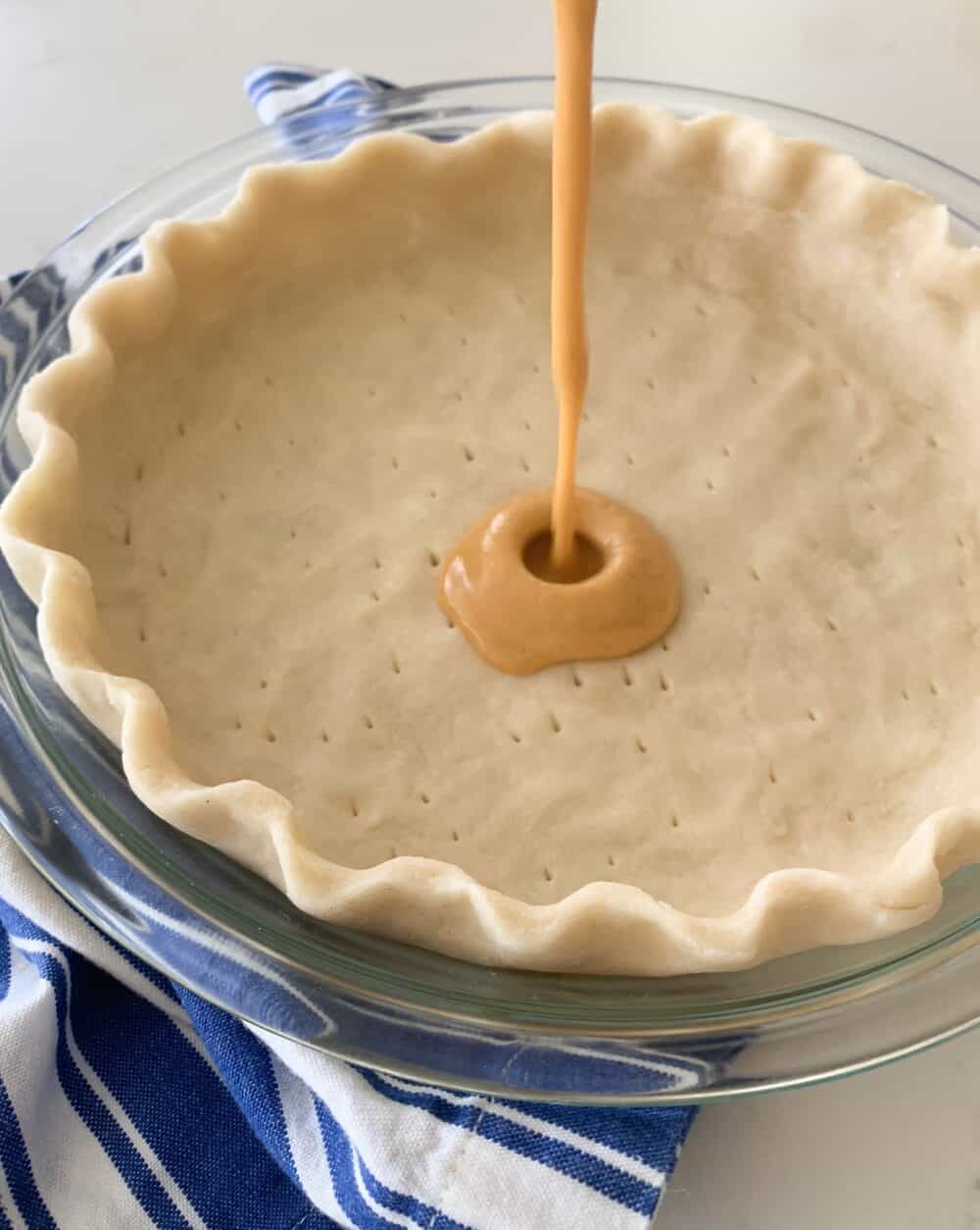 pouring pumpkin pie into pie crust to bake