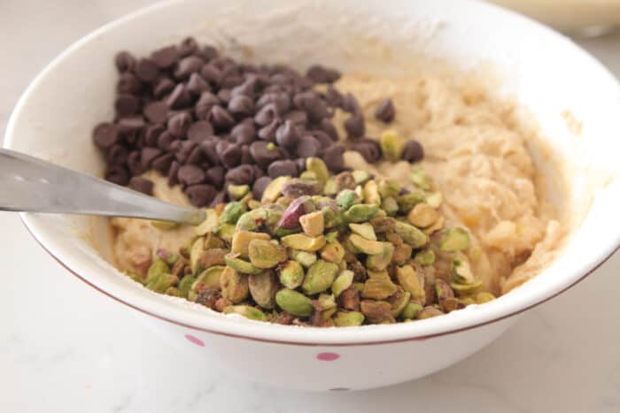 pistachio and chocolate chips added to banana bread batter in mixing bowl