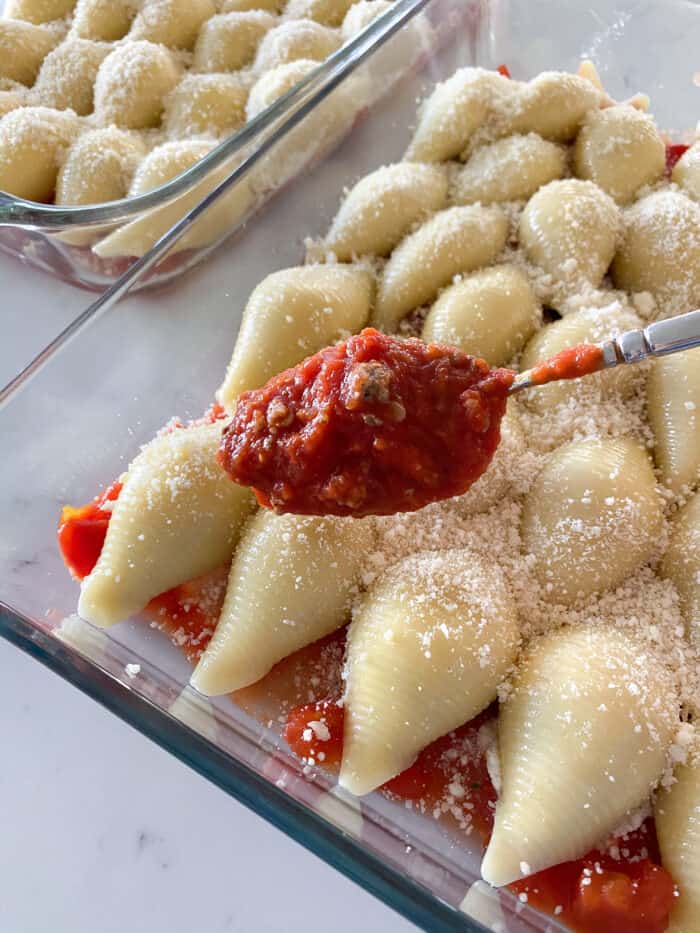 adding meat sauce to pasta shells in a baking dish