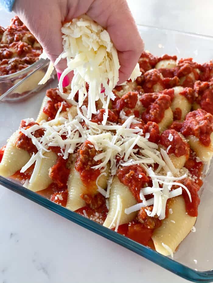 Adding cheese to pasta shells covered in meat sauce