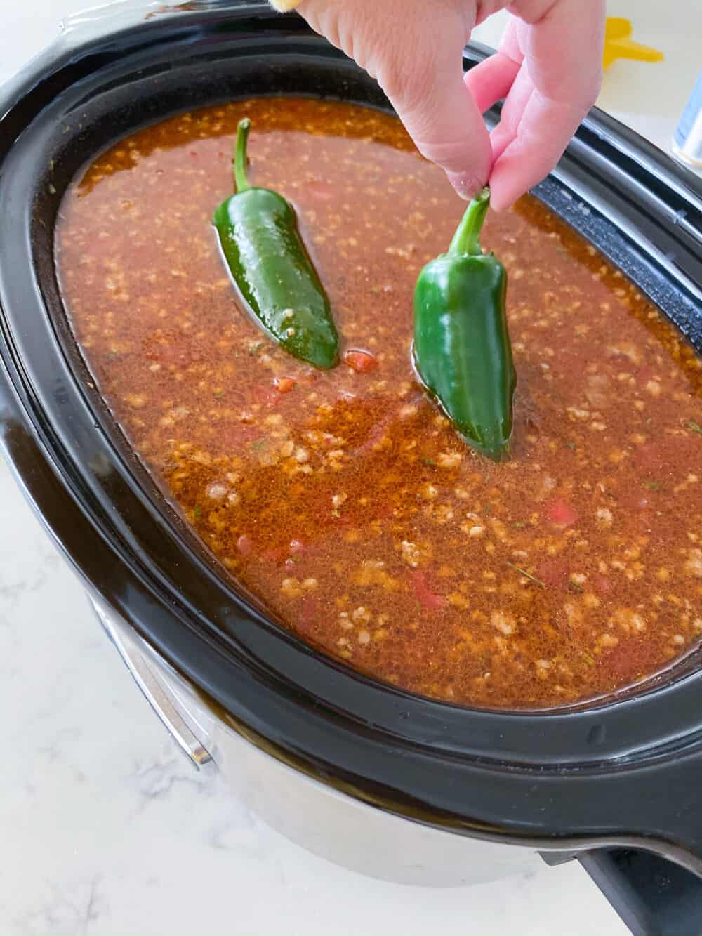 adding jalapeños to crockpot of homemade chili recipe