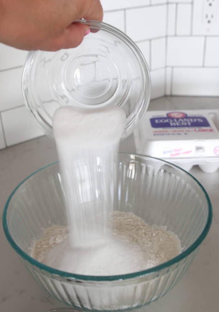 pouring sugar into a mixing bowl for chocolate chip pancakes