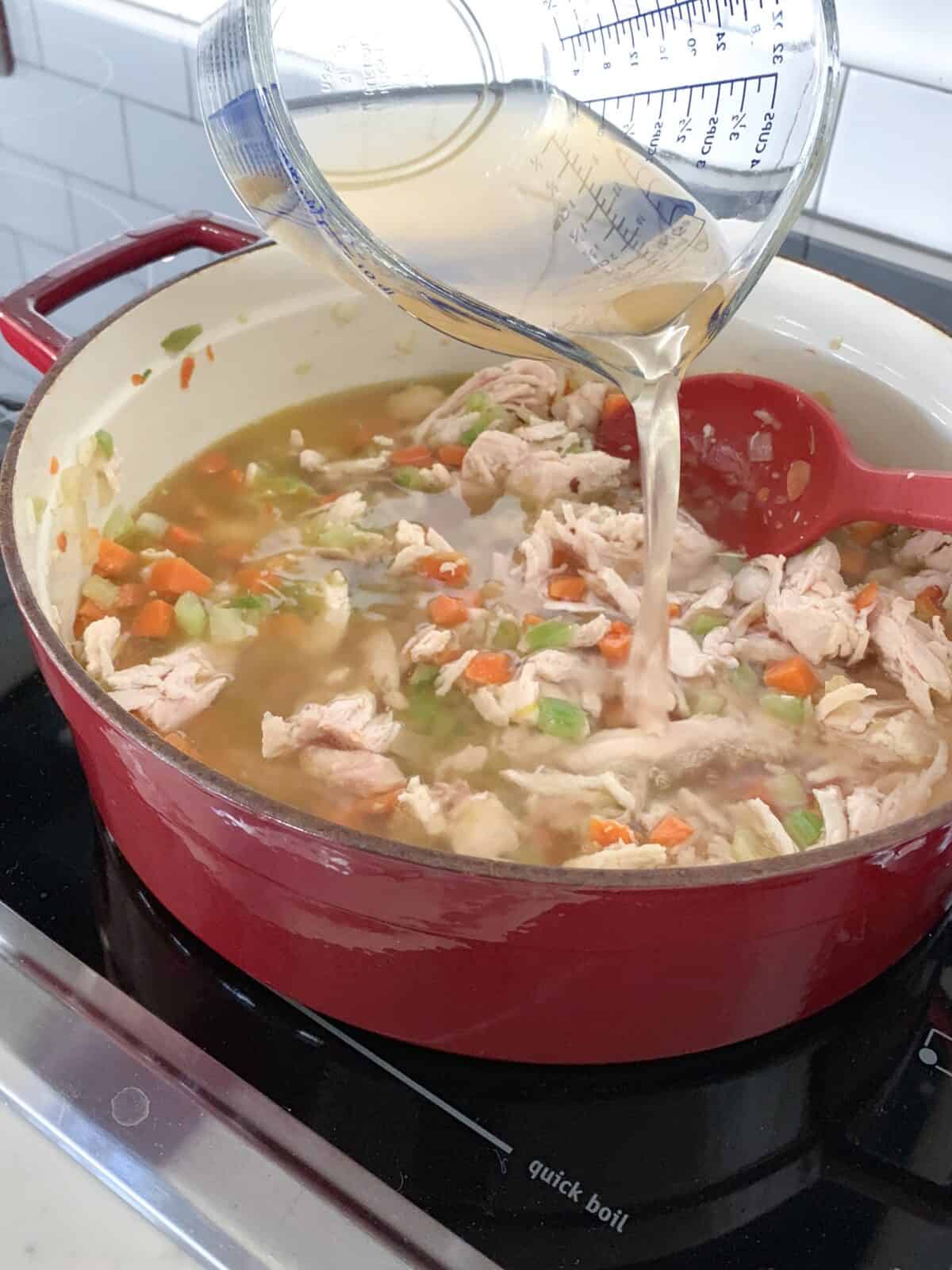 adding chicken broth to soup pot