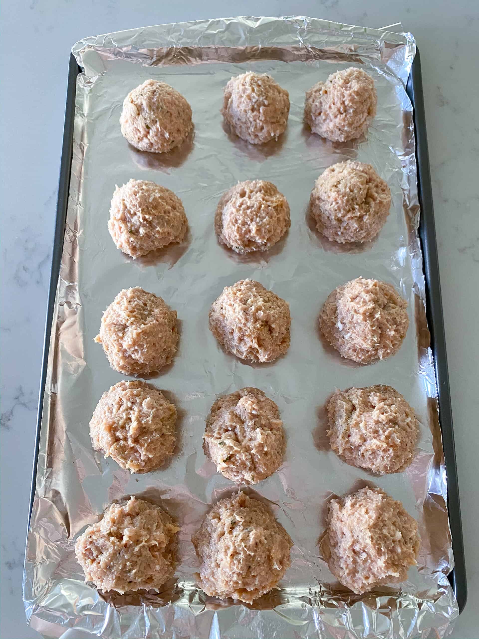 Raw chicken meatballs on a baking sheet ready to be cooked.