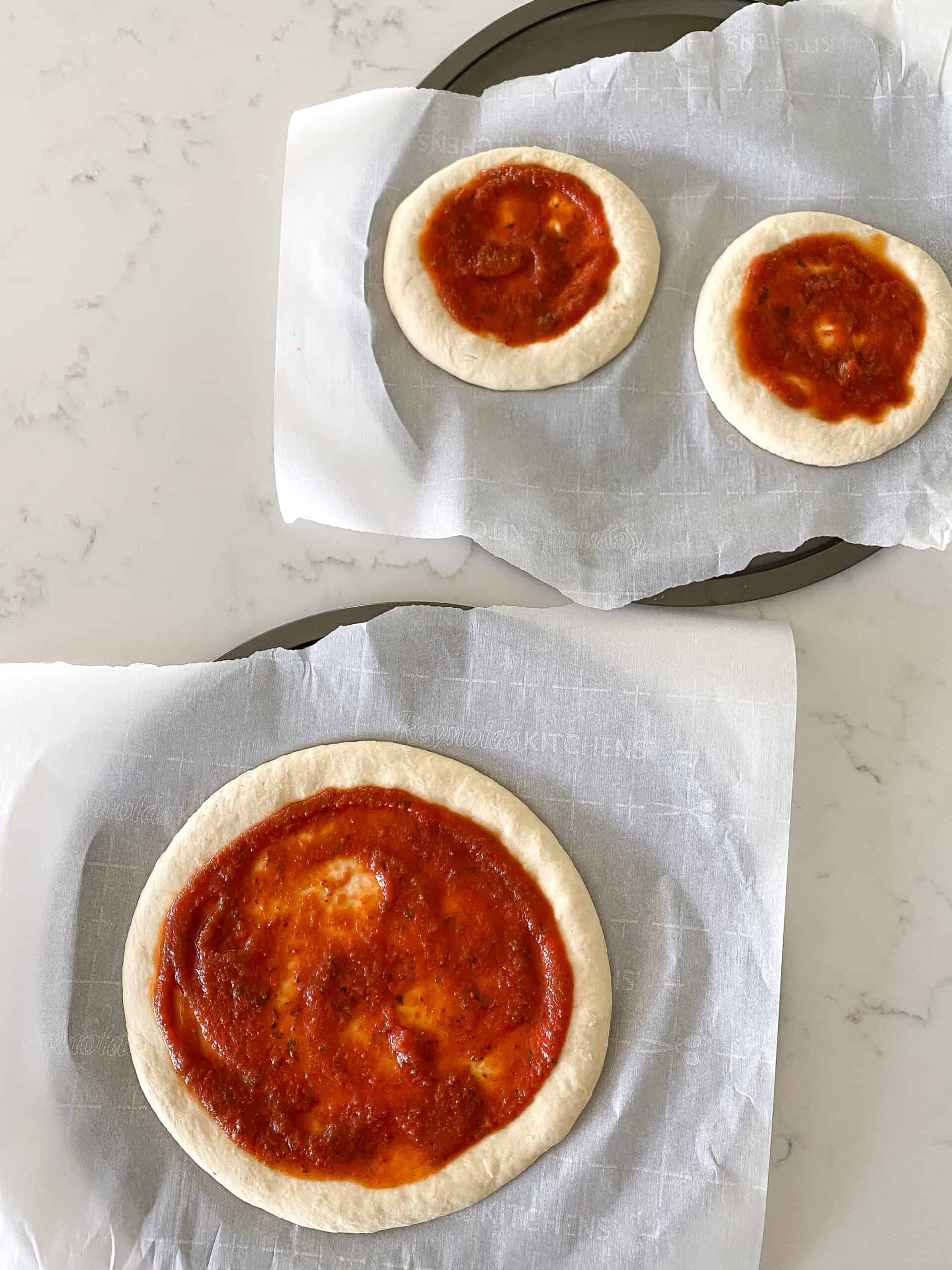 spreading pizza sauce over pizza dough