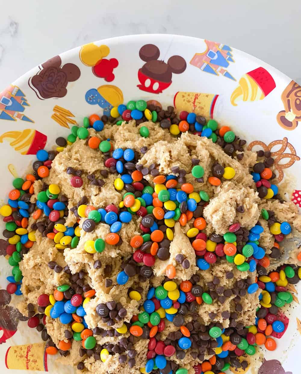 adding ingredients to bowl for m&m cookie bars