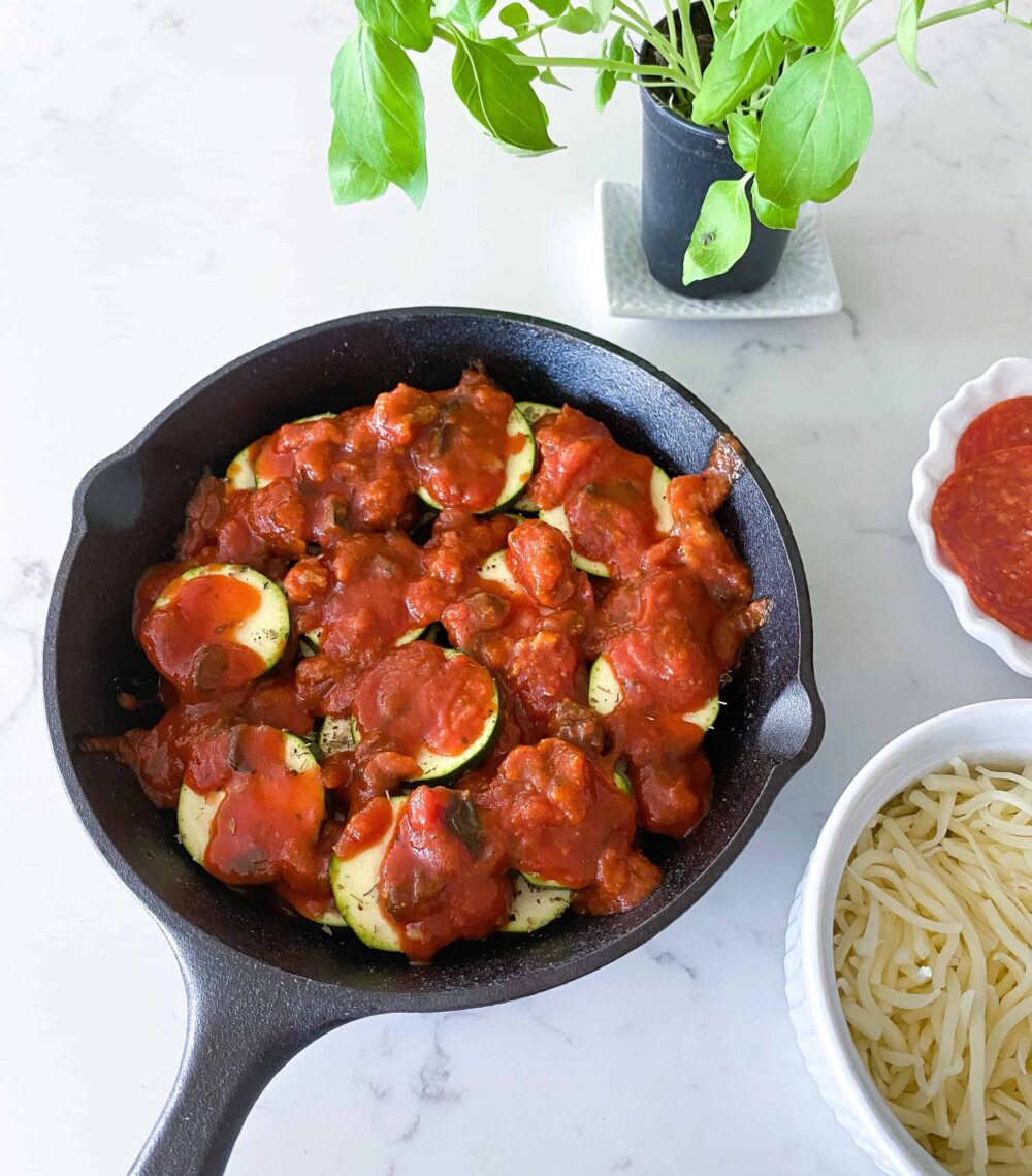 layering pasta sauce over zucchini slices in cast iron skillet