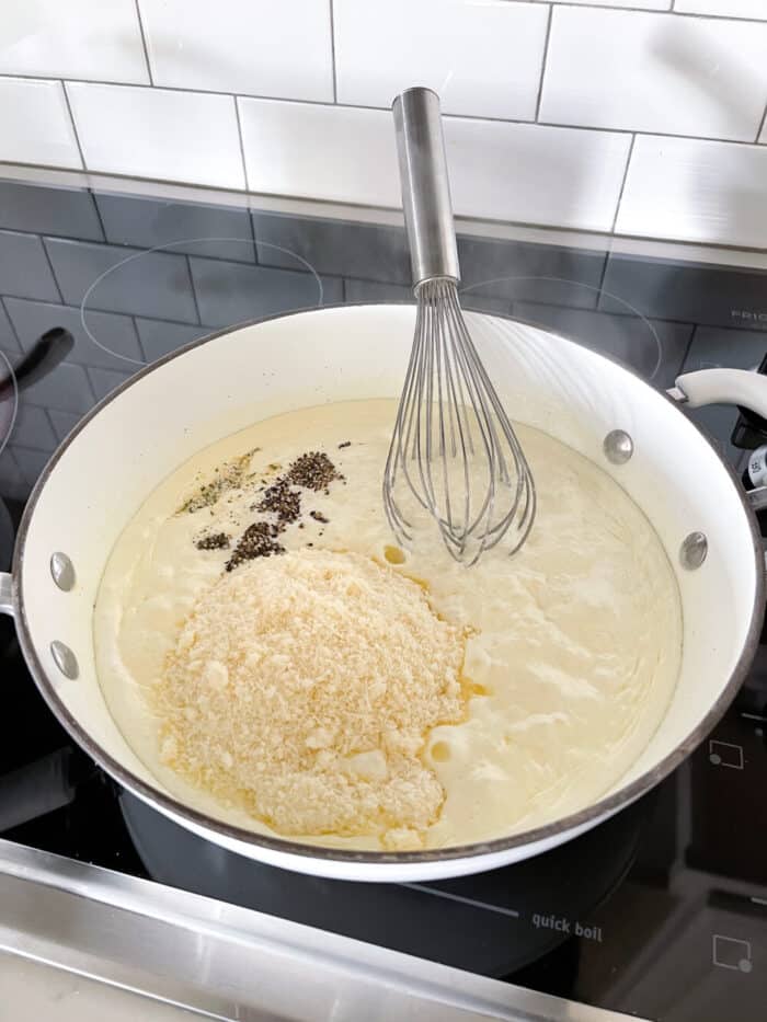 adding parmesan cheese and seasonings to pot of alfredo sauce