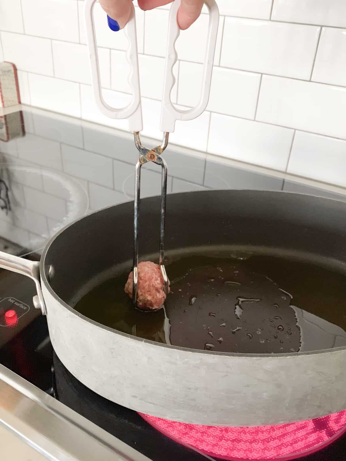 placing meatball into hot pan to cook