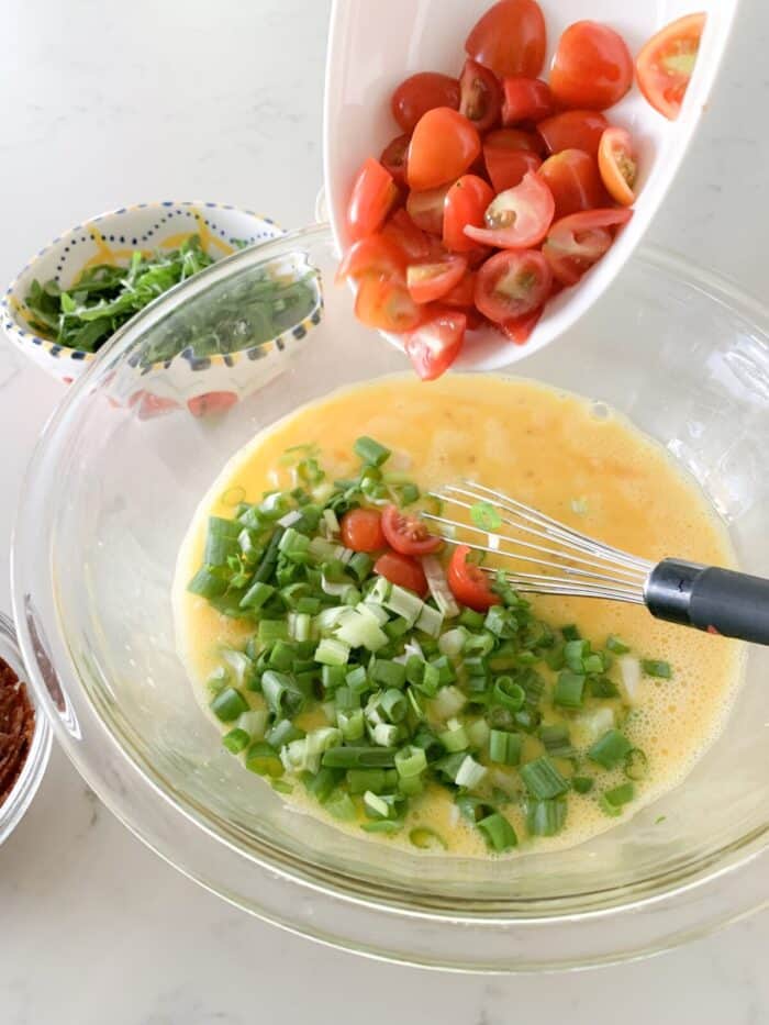 adding tomatoes and green onion to eggs in large mixing bowl