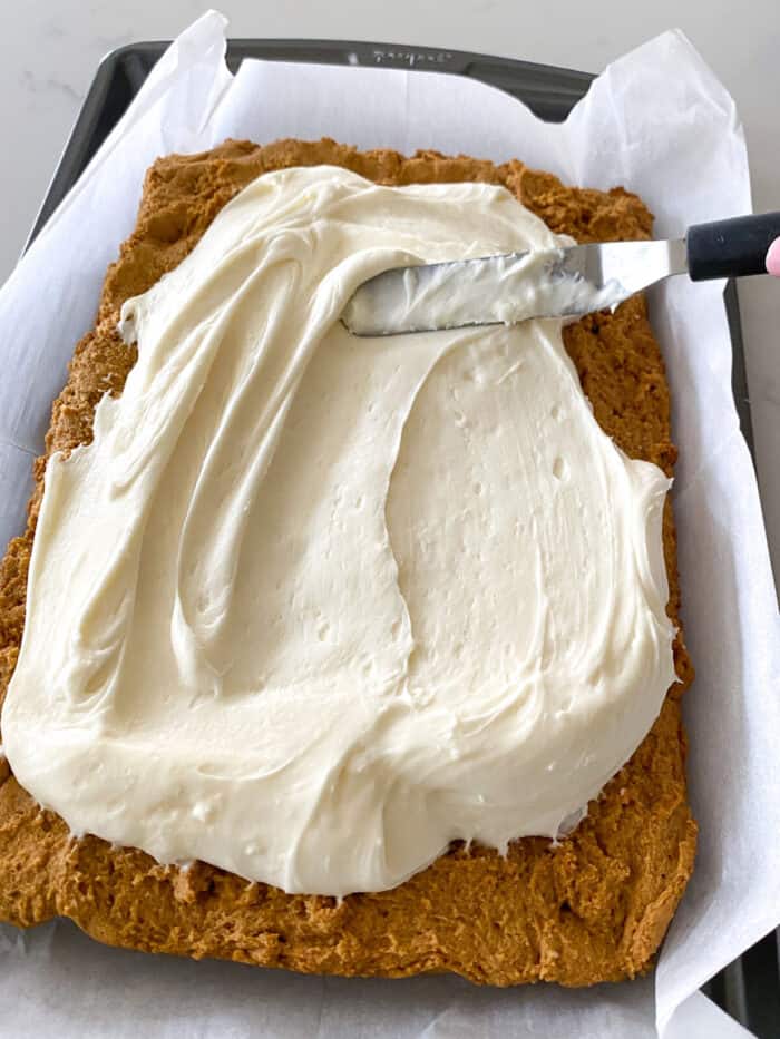 spreading cream cheese frosting over peanut butter cheesecake bars