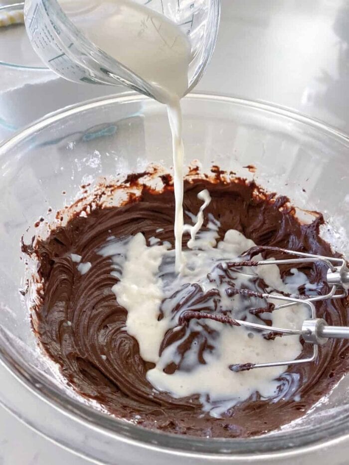 adding milk to chocolate frosting in mixing bowl