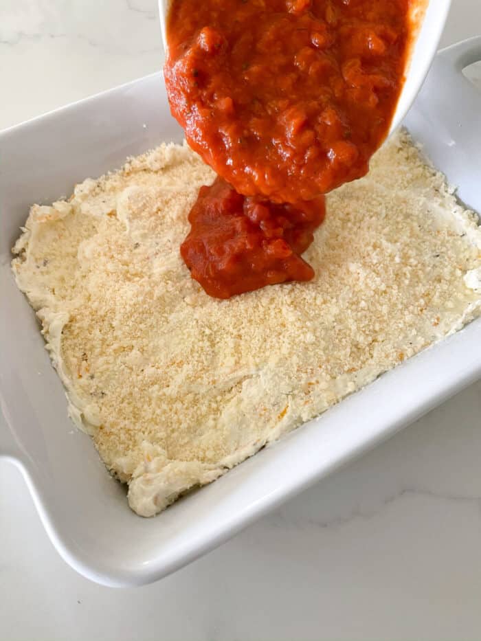 adding pizza sauce to cream cheese layer in baking dish