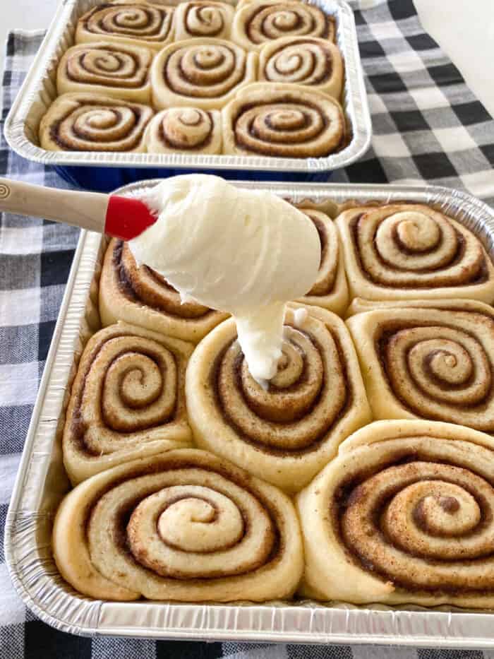spreading cream cheese frosting on warm baked cinnamon rolls
