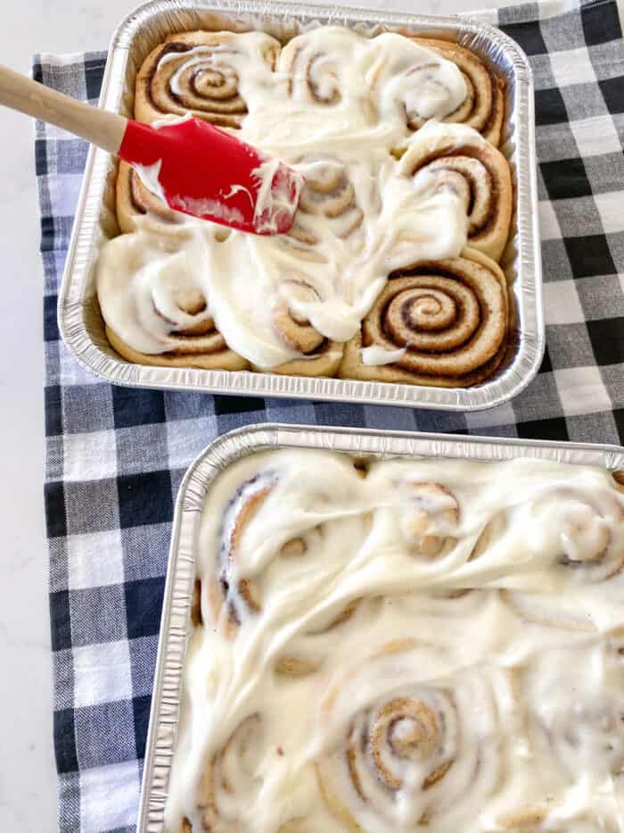 spreading cream cheese frosting on warm baked cinnamon rolls