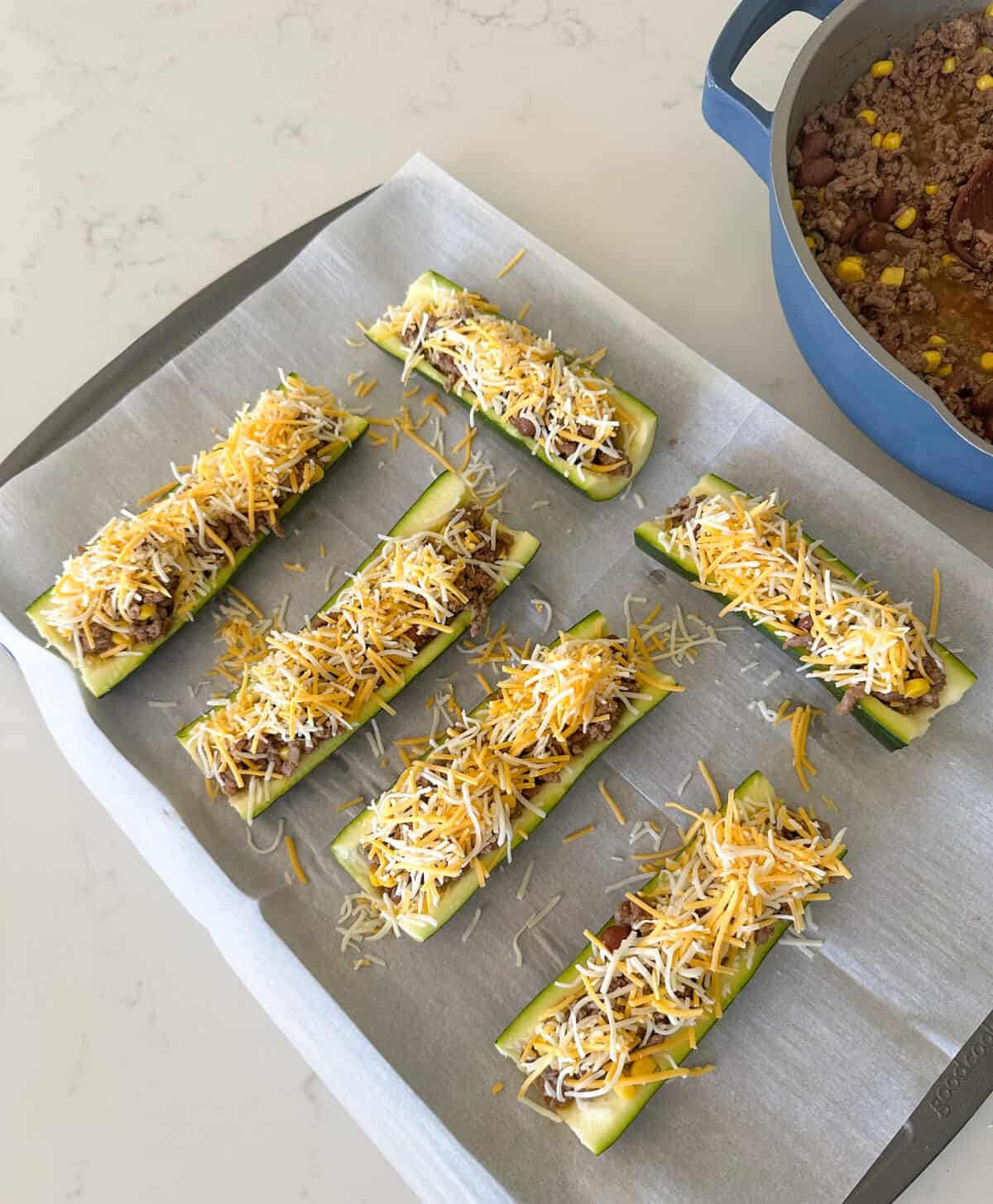 zucchini boats topped with beef filling and shredded cheese ready for oven