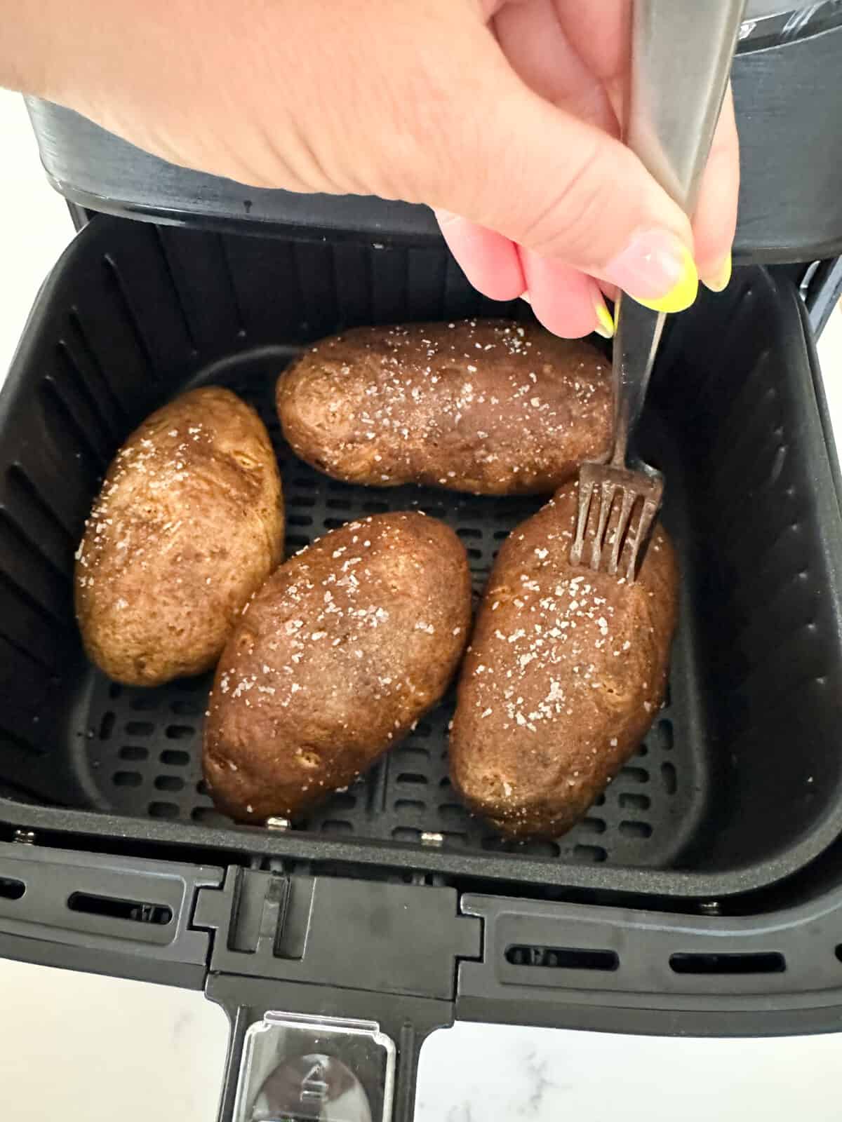 potatoes inside air fryer checking doneness with a fork