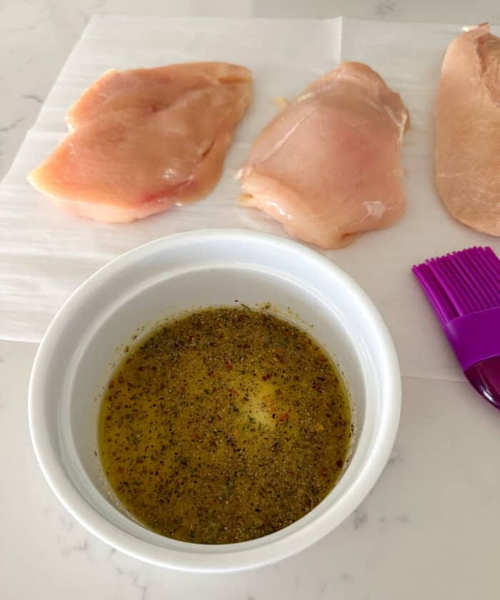 oil and seasonings in bowl with chicken breast on parchment paper