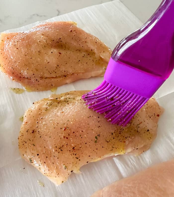 brushing oil and seasoning over raw chicken breast