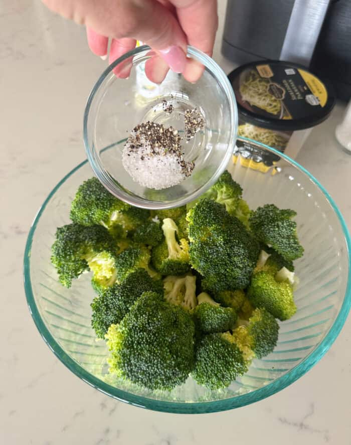 adding seasoning to bowl of broccoli florets