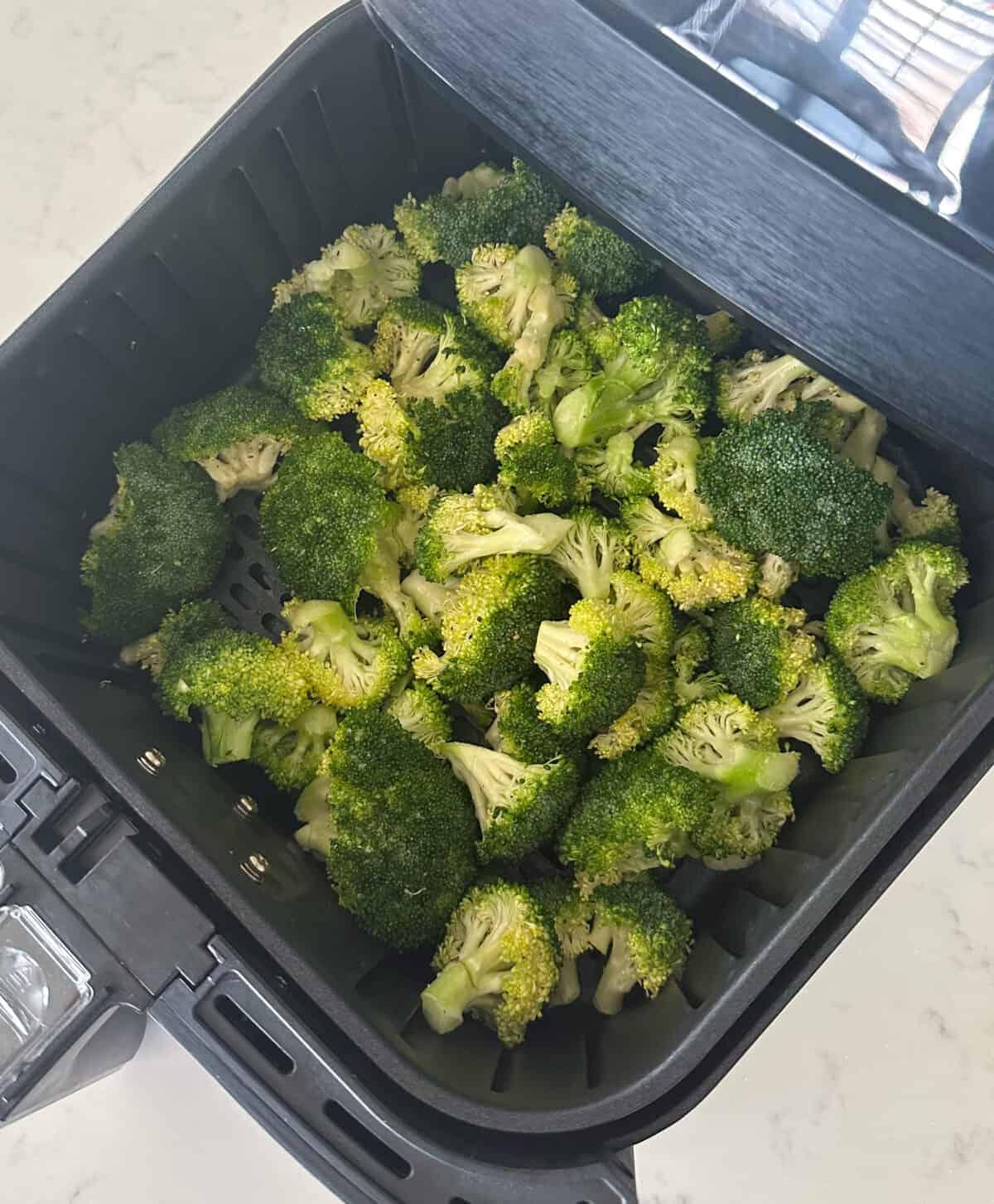 uncooked broccoli seasoned placed in basket of air fryer