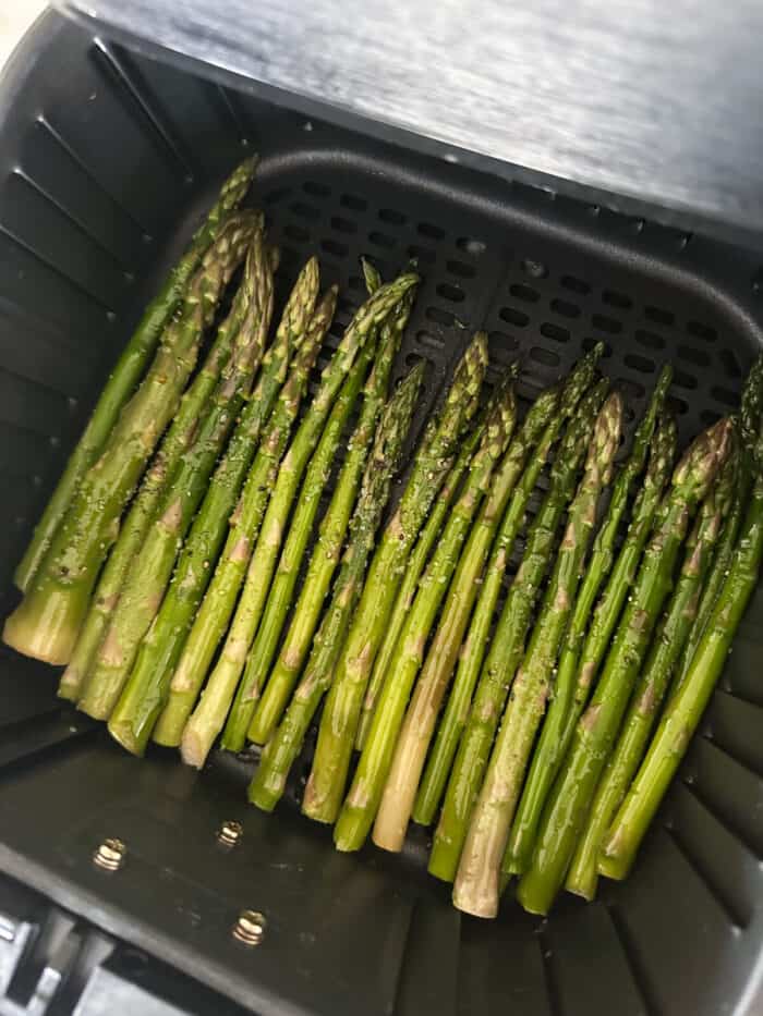 seasoned asparagus in air fryer basket ready to cook