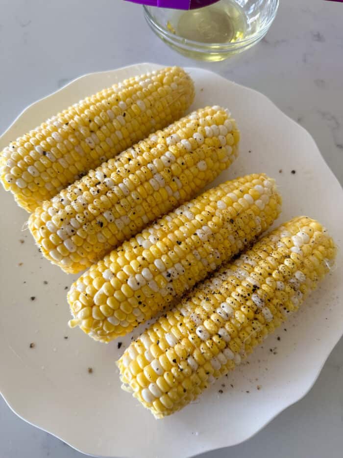 corn on the cob on plate with salt pepper and oil