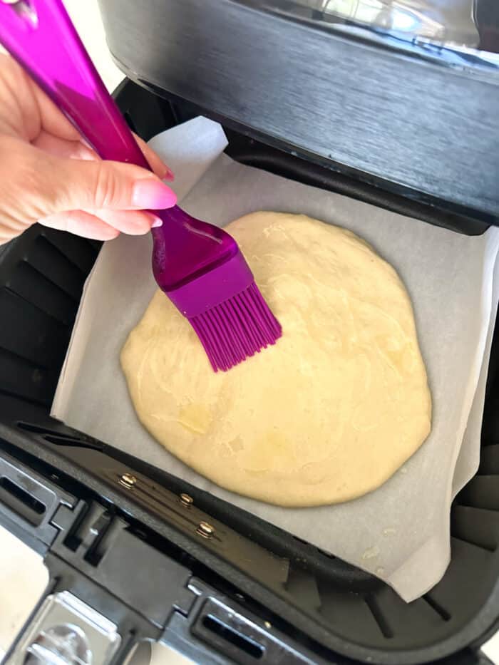 brushing pizza dough round with olive oil