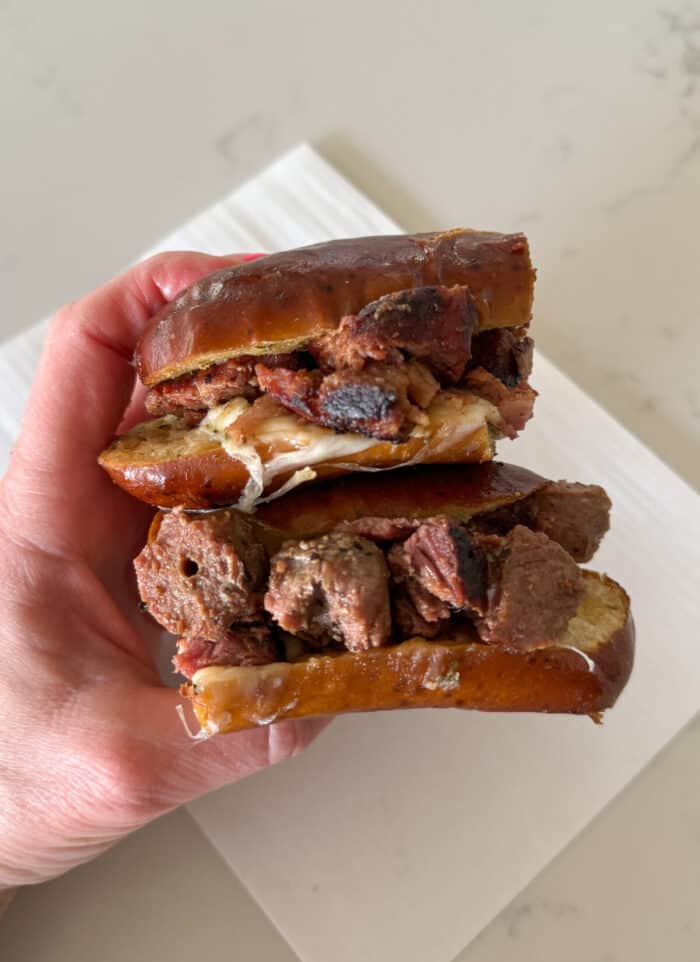 steak sandwich cut in half in cheesy garlic pretzel roll