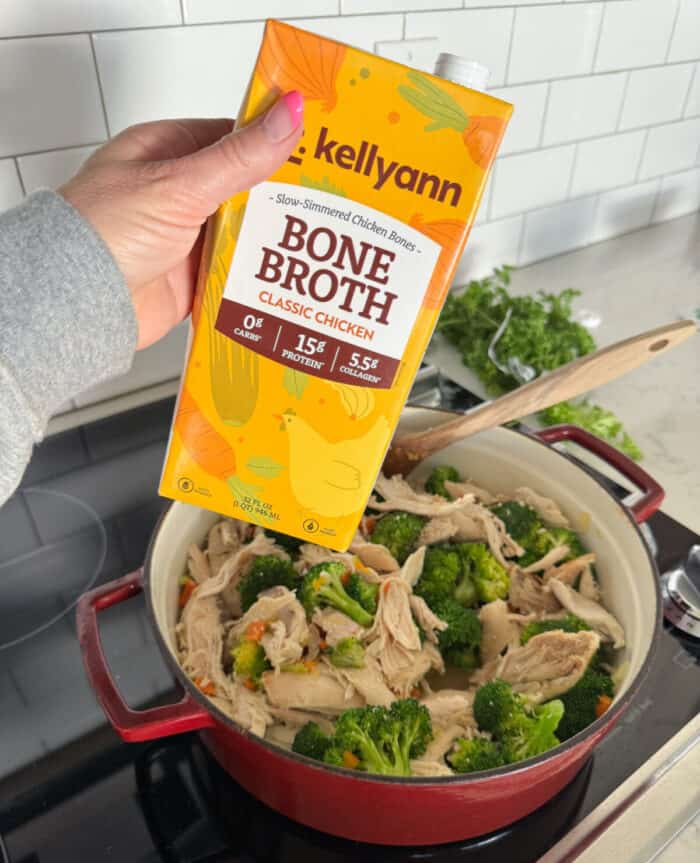 adding bone broth to pot of soup with chicken and vegetables