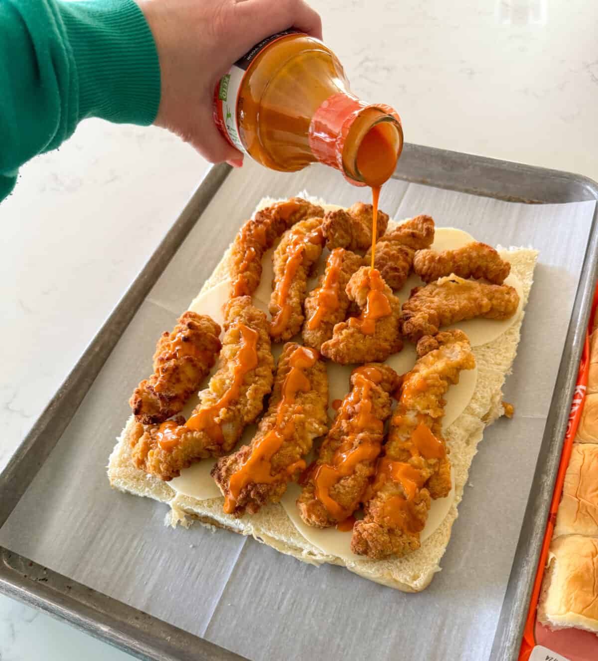 pouring buffalo sauce over chicken tenders