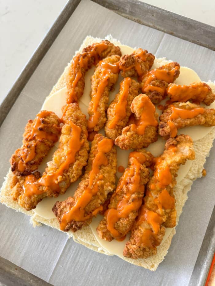 buffalo sauce drizzled over chicken tenders on top of rolls