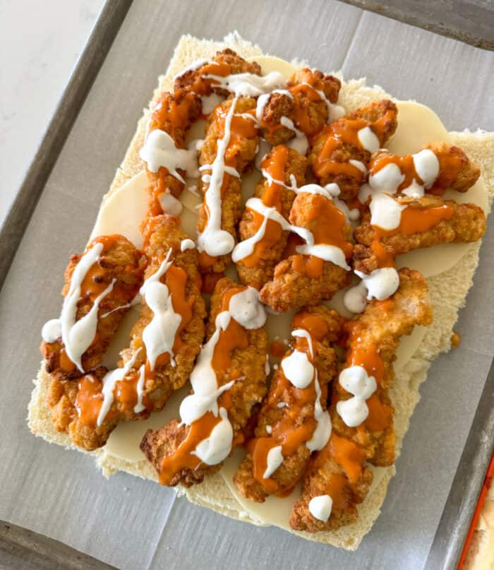 ranch dressing drizzled over chicken tenders on top of rolls